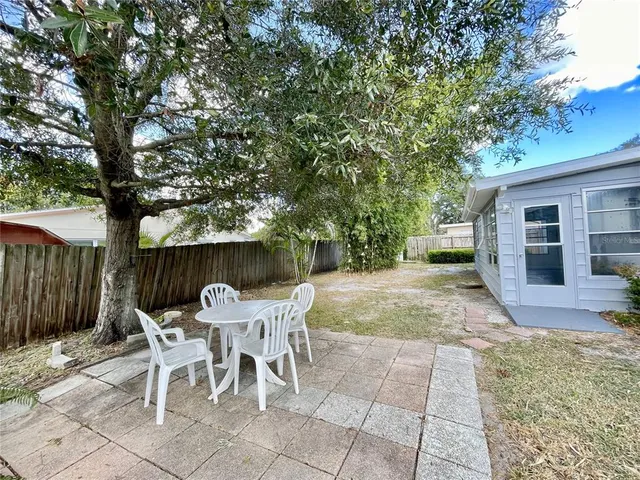 a view of a backyard with table and chairs potted plants and large tree