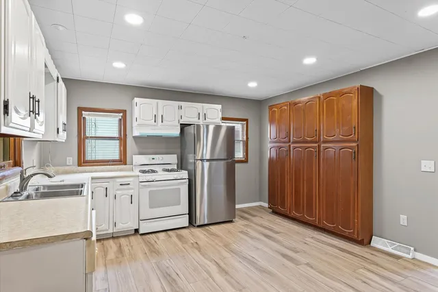 a kitchen with stainless steel appliances granite countertop a refrigerator a sink dishwasher a stove and white countertops with wooden floor