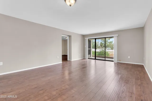 a view of an empty room with wooden floor and a kitchen