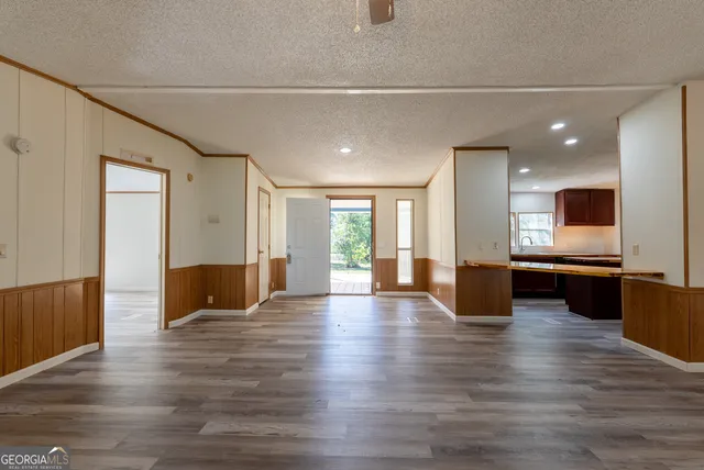 a view of an empty room with wooden floor and a kitchen
