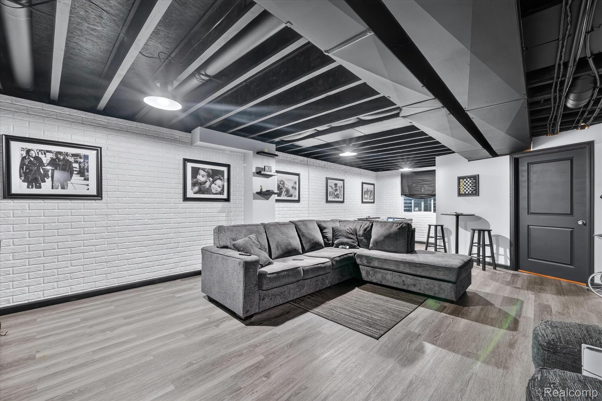 5382 Rural Terrace Waterford, MI 48329 - Photo 27 of 35 Spacious entertainment area featuring a white brick-finish accent wall, wood-finish flooring, recessed lighting, and a painted exposed ceiling with ductwork
