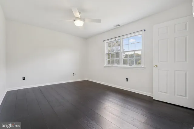 an empty room with wooden floor fan and windows