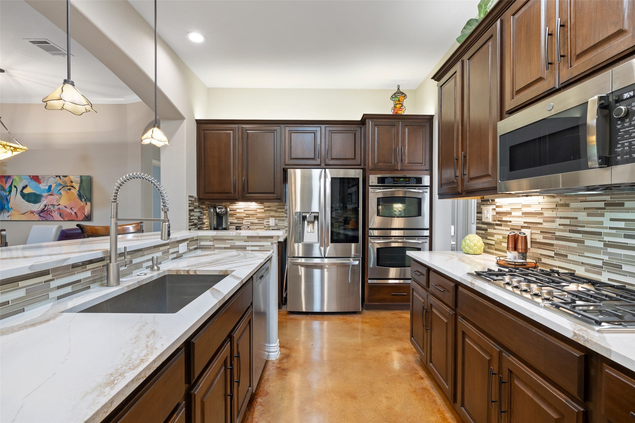 15208 Nightingale Lane Austin, TX 78734 - Photo 12 of 40 Kitchen featuring stainless steel appliances, dark wood finish cabinetry, concrete flooring, light stone counters, and ornamental molding