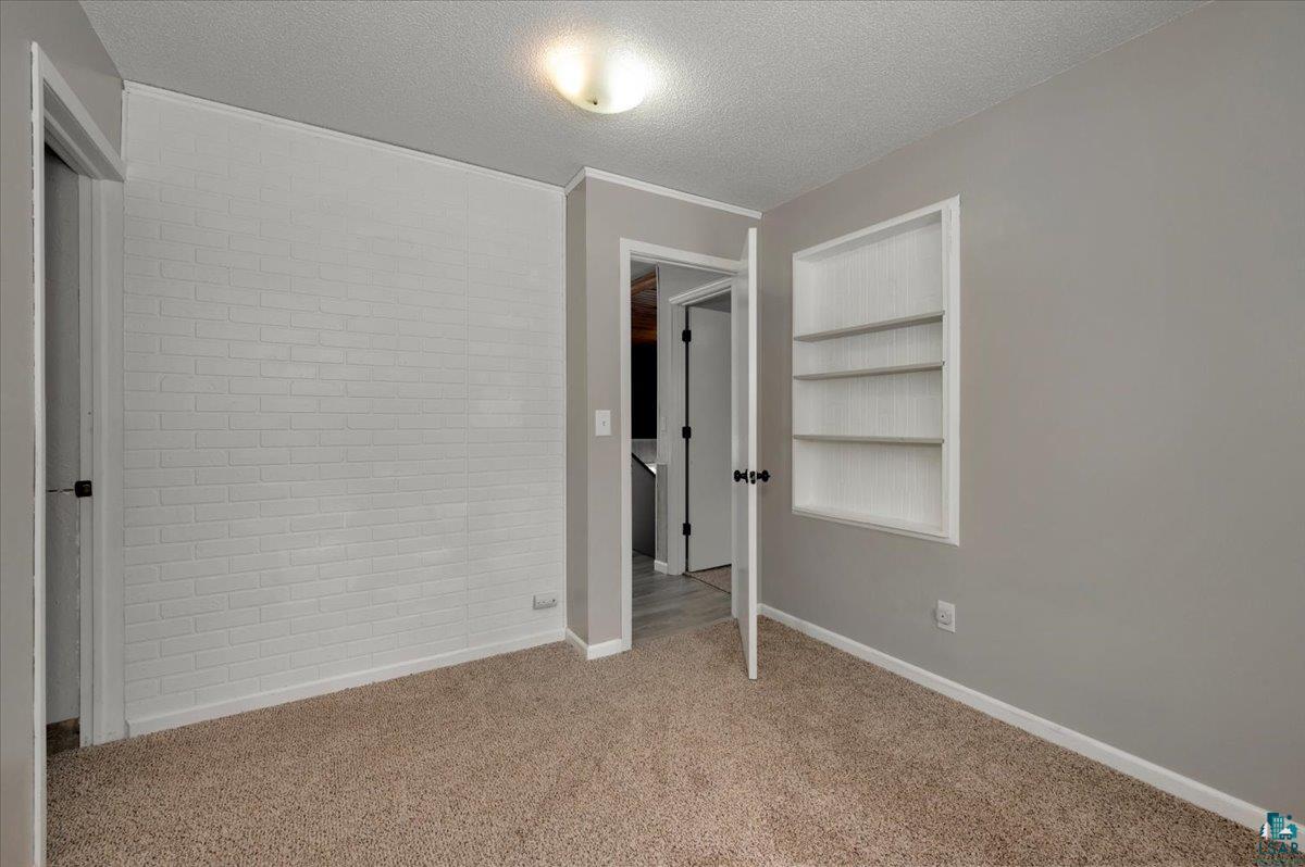 1146 Two Harbors Road Two Harbors, MN 55616 - Photo 15 of 39 Unfurnished bedroom featuring brick wall, a textured ceiling, and light colored carpet