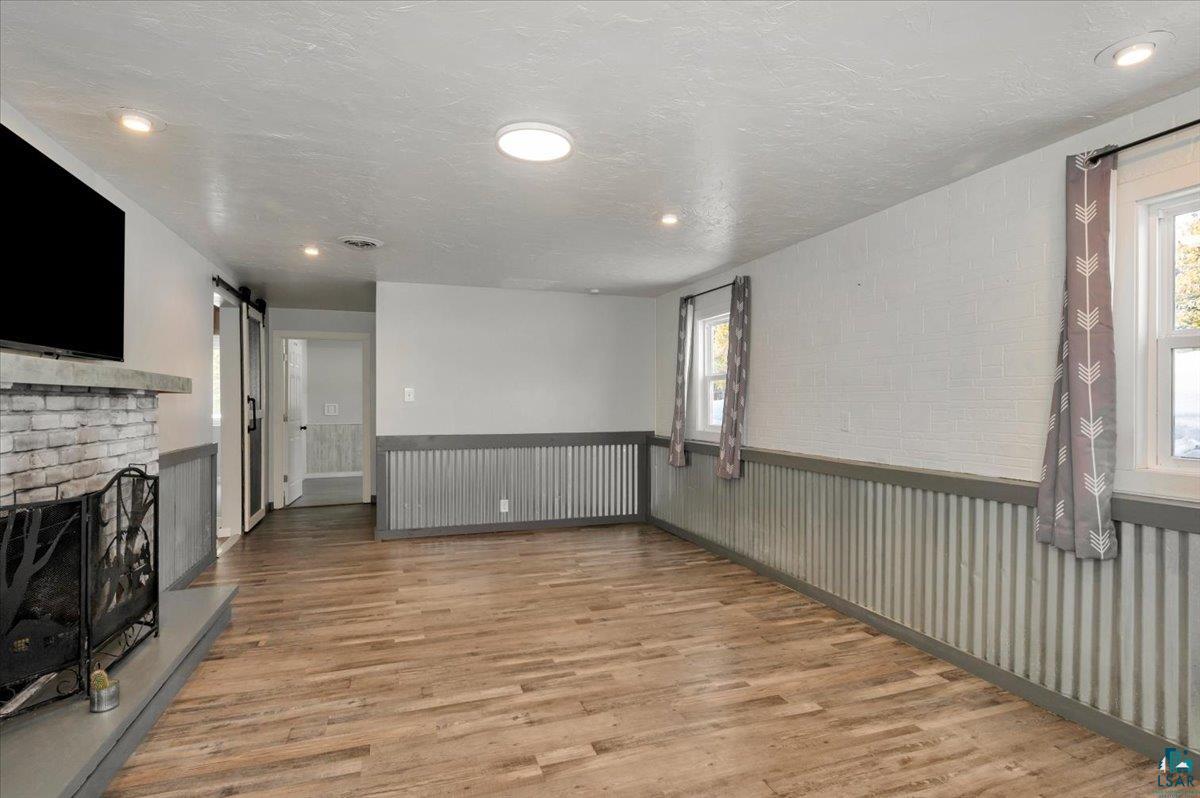 1146 Two Harbors Road Two Harbors, MN 55616 - Photo 19 of 39 Unfurnished living room with a barn door, wainscoting, light wood-style floors, a brick fireplace, and a textured ceiling