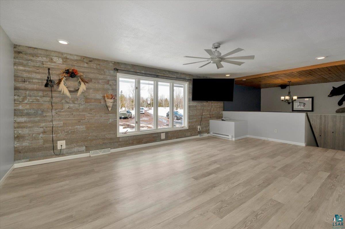 1146 Two Harbors Road Two Harbors, MN 55616 - Photo 6 of 39 Unfurnished living room with ceiling fan, light wood-style flooring, wood walls, hanging lights, and a baseboard heating unit