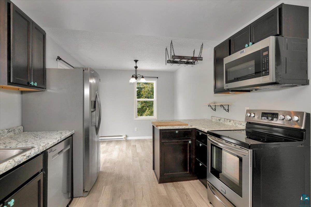 1146 Two Harbors Road Two Harbors, MN 55616 - Photo 8 of 39 Kitchen featuring stainless steel appliances, a peninsula, light wood-type flooring, pendant lighting, and a baseboard heating unit