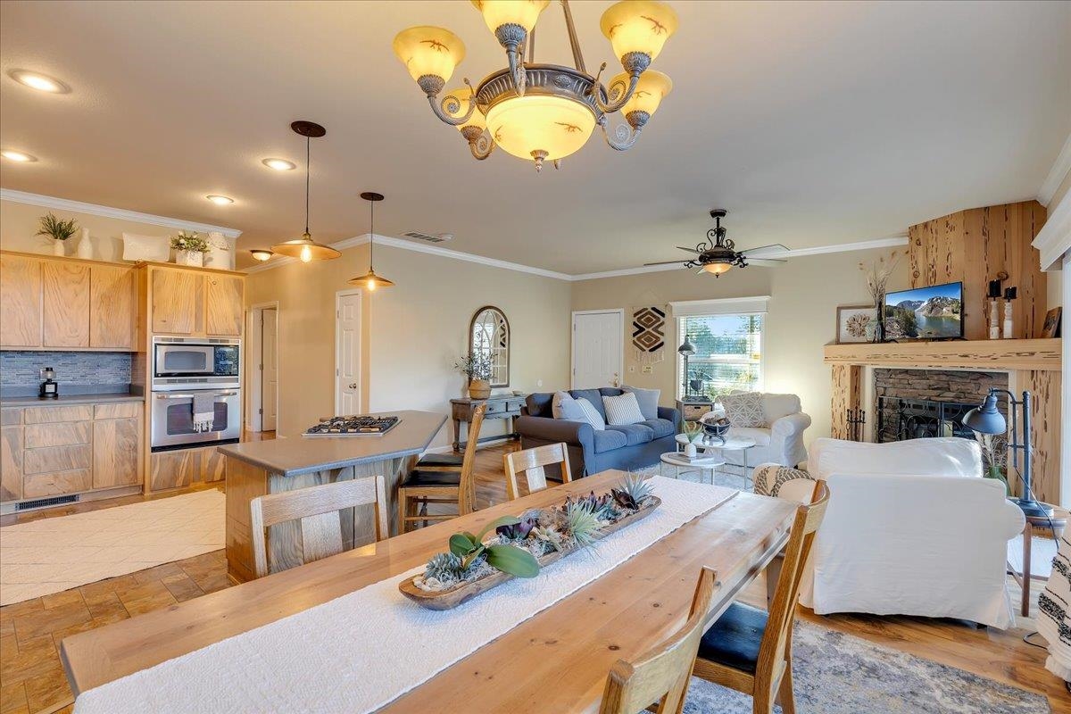 22389 Parrotts Ferry Road Columbia, CA 95310 - Photo 42 of 60 Dining space with crown molding, a chandelier, a fireplace, and ceiling fan