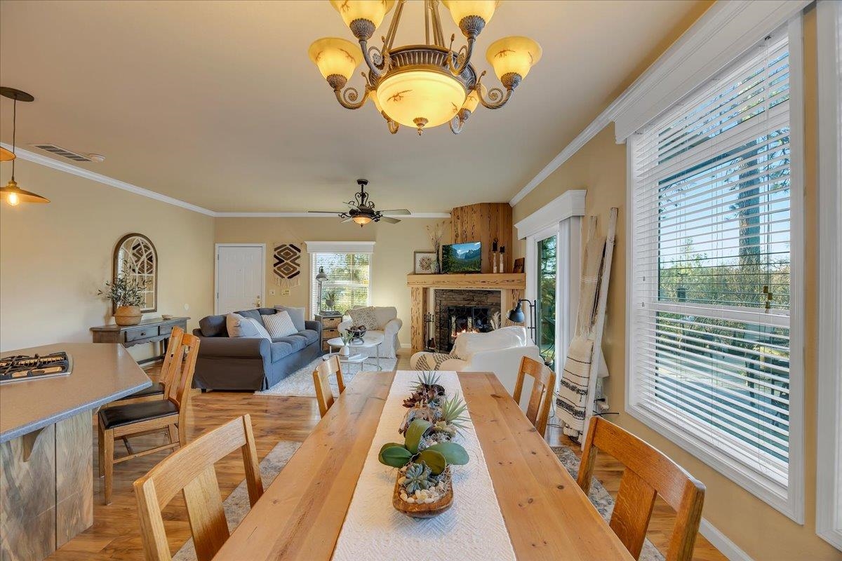 22389 Parrotts Ferry Road Columbia, CA 95310 - Photo 43 of 60 Dining space featuring light wood-style flooring, crown molding, a fireplace, a chandelier, and a ceiling fan