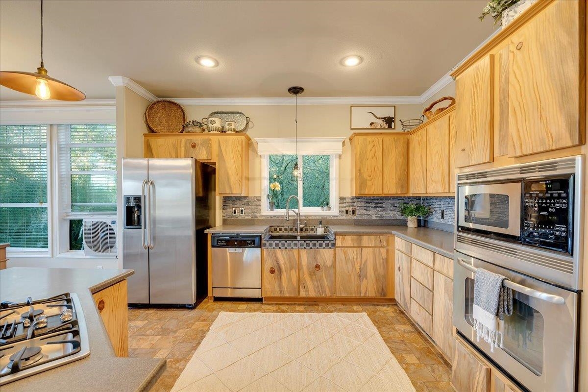 22389 Parrotts Ferry Road Columbia, CA 95310 - Photo 45 of 60 Kitchen featuring hanging light fixtures, ornamental molding, stainless steel appliances, light brown cabinets, and tasteful backsplash
