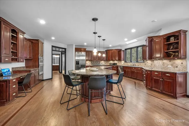 a kitchen with stainless steel appliances granite countertop a stove top oven a refrigerator a sink and chairs