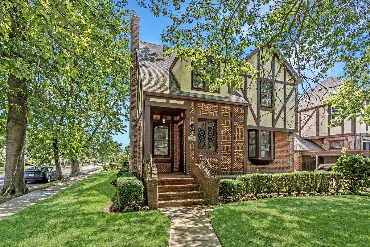 Tudor home with a front yard, brick siding, roof with shingles, and stucco siding