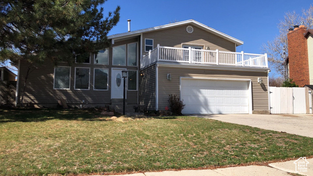 View of front facade featuring a balcony, driveway, an attached garage, a front yard, and a gate
