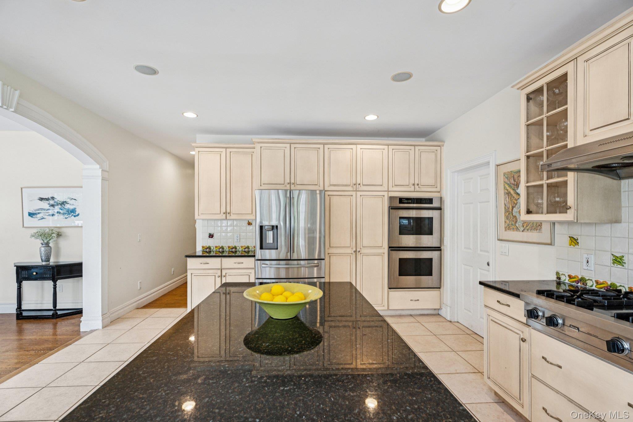 12 Laila Lane Remsenburg, NY 11960 - Photo 17 of 50 Kitchen featuring granite countertops, a spacious island, glass-inset custom cabinetry, an eat-in dining area, recessed lighting, light-patterned tile flooring.