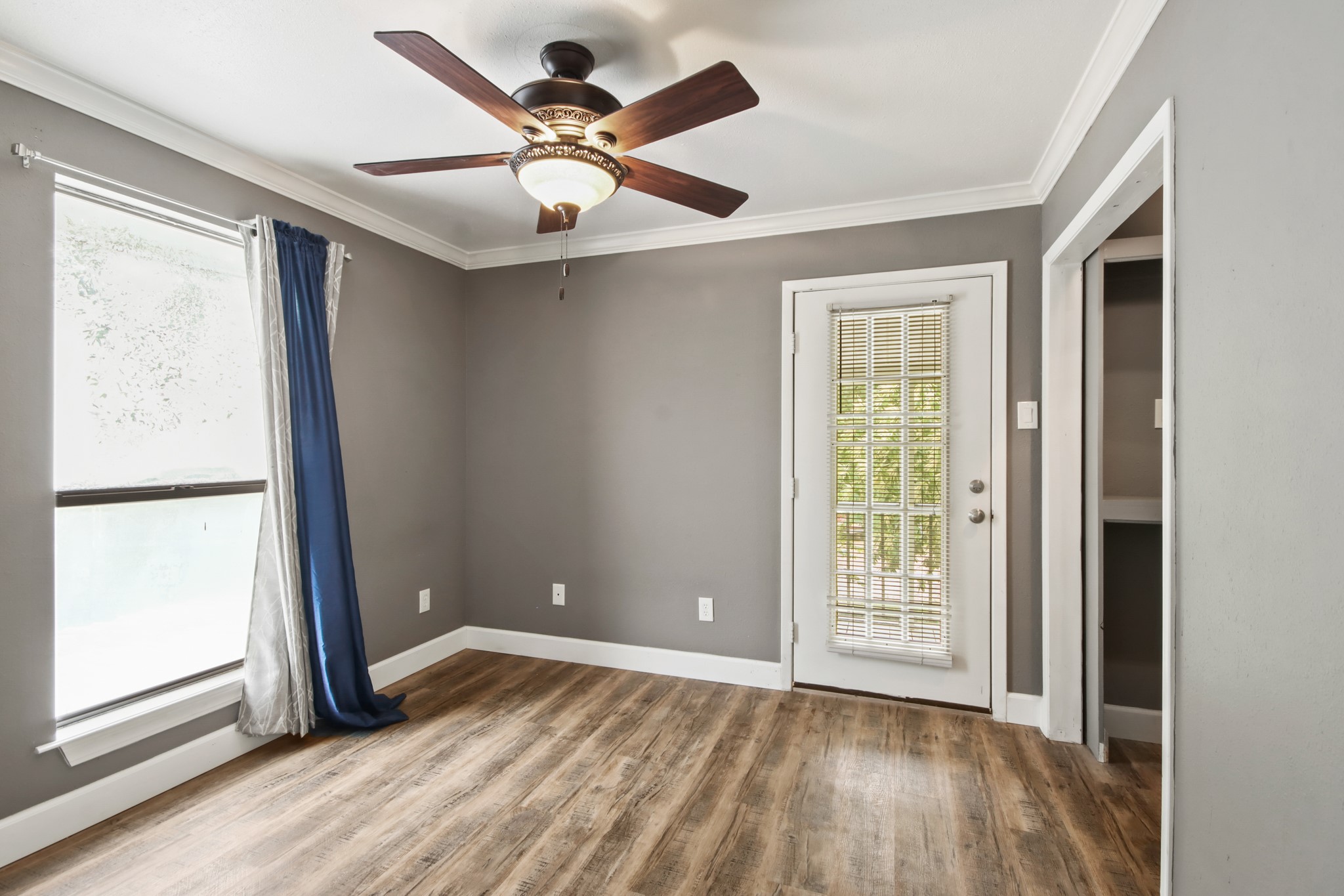 35 Susan Drive Cleveland, TX 77327 - Photo 21 of 33 This room features elegant gray walls, wood flooring, and a ceiling fan. It includes a window with blue curtains and a door with blinds, providing plenty of natural light.