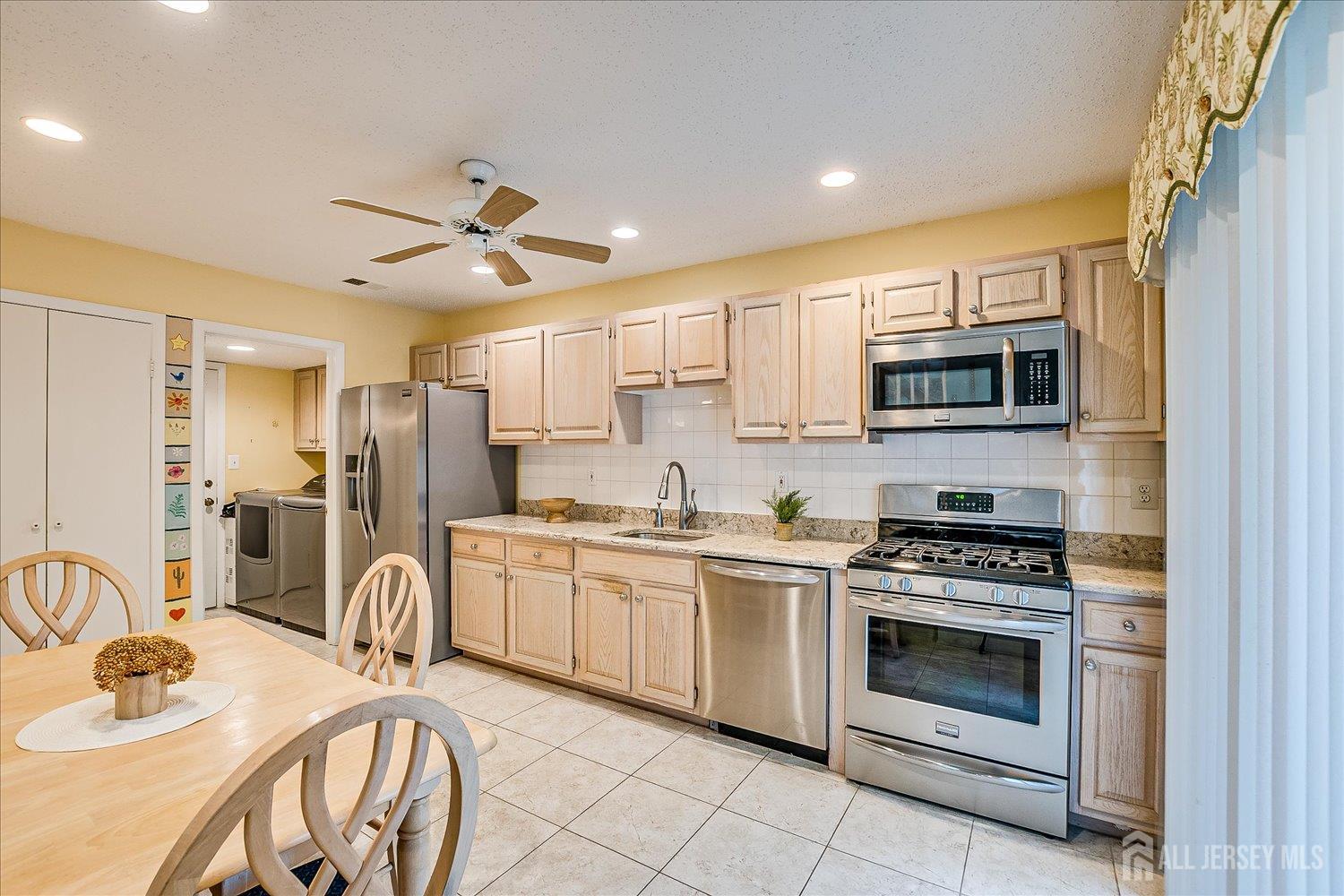 75 Kelly Drive Edison, NJ 08820 - Photo 15 of 41 a kitchen with stainless steel appliances granite countertop a stove top oven a sink dishwasher a dining table and chairs with wooden cabinets