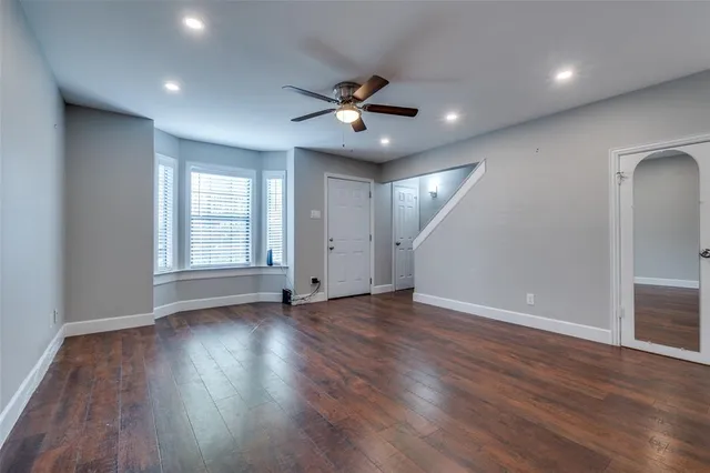 an empty room with wooden floor a ceiling fan and windows