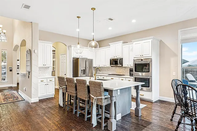 a kitchen with stainless steel appliances a dining table chairs refrigerator and microwave