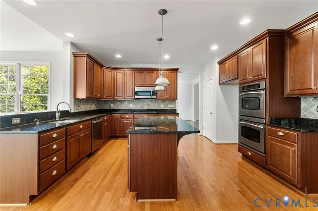 a kitchen with stainless steel appliances granite countertop a refrigerator a sink dishwasher a stove and a dining table with wooden floor