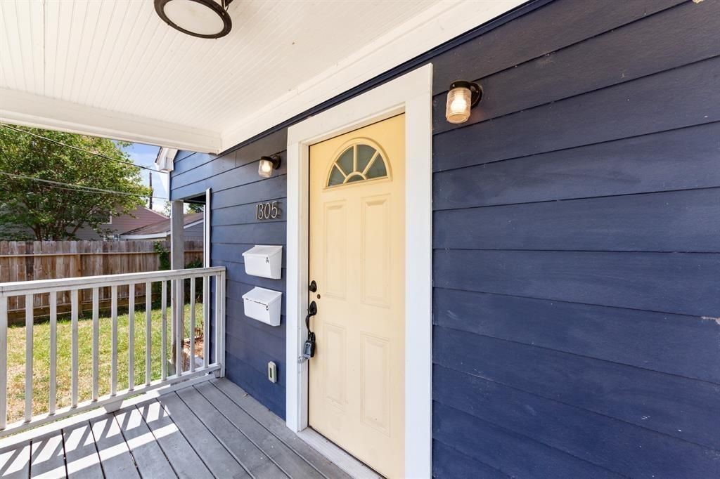 1305 Idylwild Street Houston, TX 77009 - Photo 2 of 31 Charming front porch with a classic navy exterior, a welcoming yellow door, and outdoor lighting. Features include two white mailboxes and a fenced yard, offering a cozy entryway to your future home.