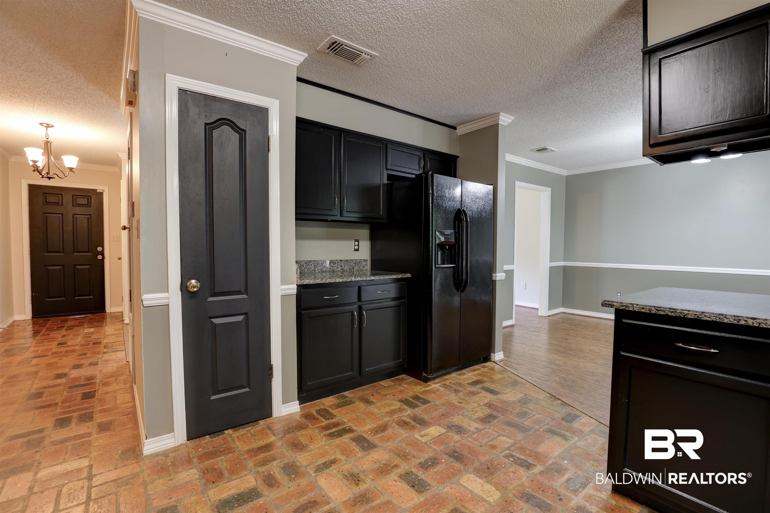 492 Ridgewood Drive Daphne, AL 36526 - Photo 6 of 17 Kitchen with crown molding, a textured ceiling, an inviting chandelier, dark stone counters, and black refrigerator with ice dispenser