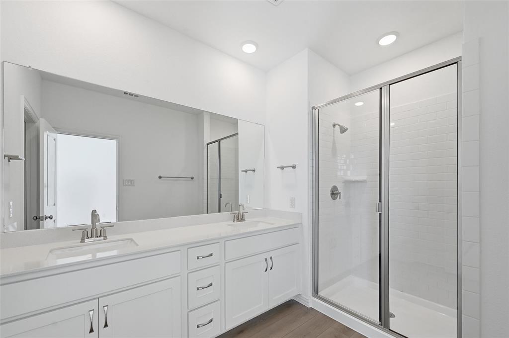 1168 Daybreak Drive, Unit 1168 Allen, TX 75013 - Photo 20 of 25 Dual vanity with undermount sinks and chrome fixtures, expansive mirror, wood-finish flooring, and a glass-enclosed shower with subway tile