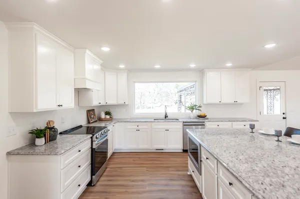 a kitchen with stainless steel appliances granite countertop a sink stove and white cabinets with wooden floor