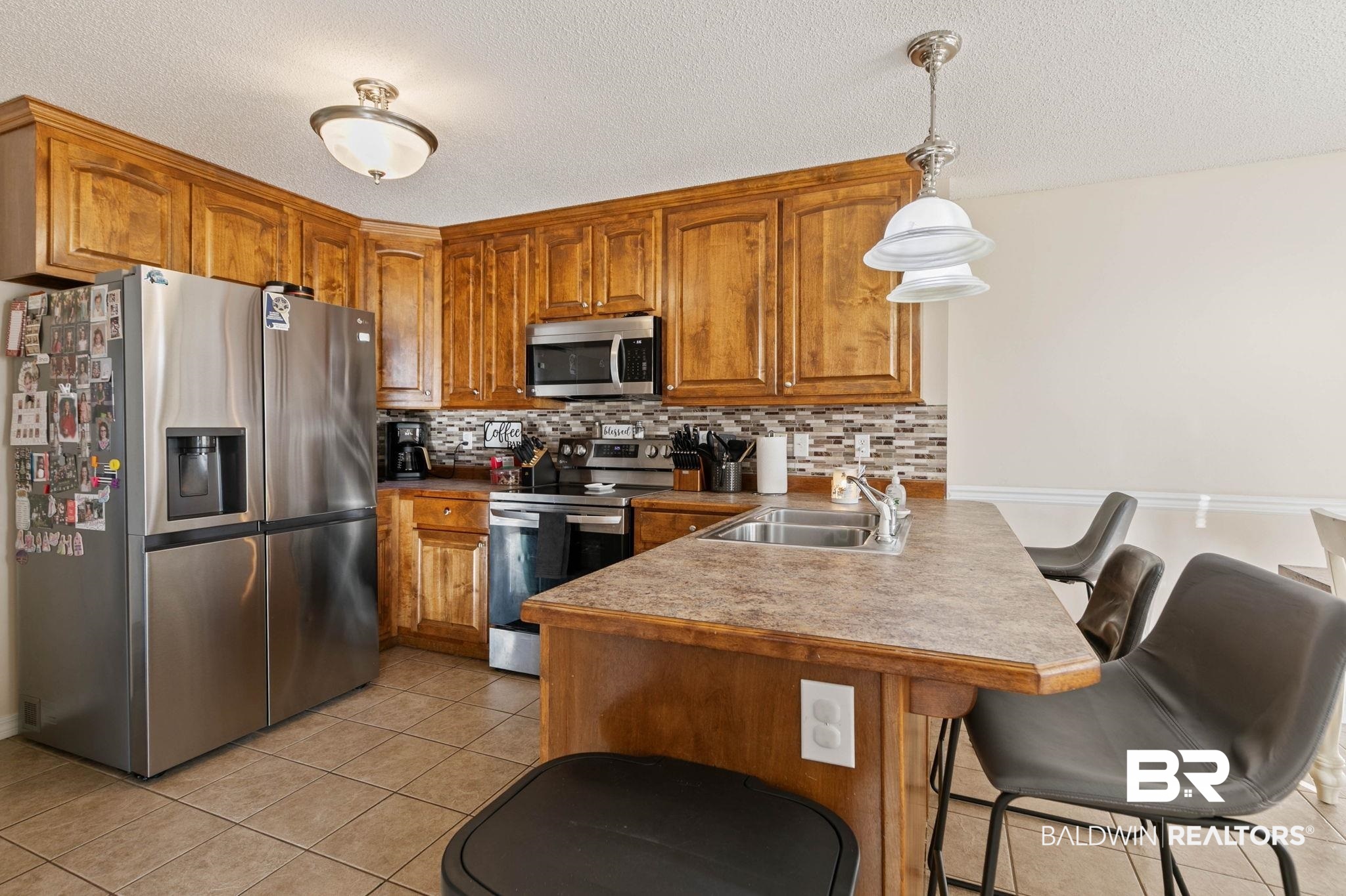 55750 Lottie Road Perdido, AL 36562 - Photo 66 of 84 Kitchen with wood finish cabinetry, stainless steel appliances, a breakfast bar, light tile patterned floors, and pendant lighting