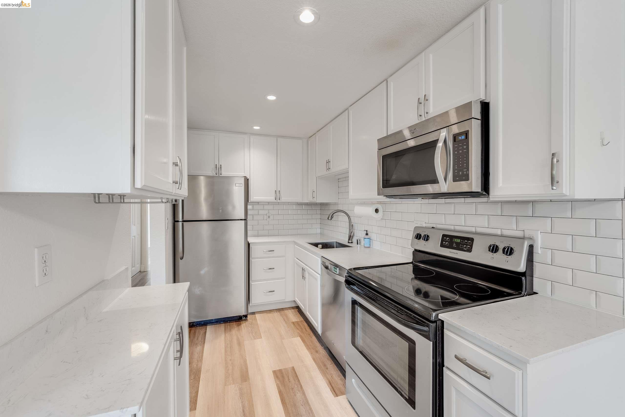 3641 Clayton Road, Unit 37 Concord, CA 94521 - Photo 1 of 1 Kitchen featuring white cabinetry, stainless steel appliances, light-toned countertops, subway tile backsplash, and wood-finish flooring