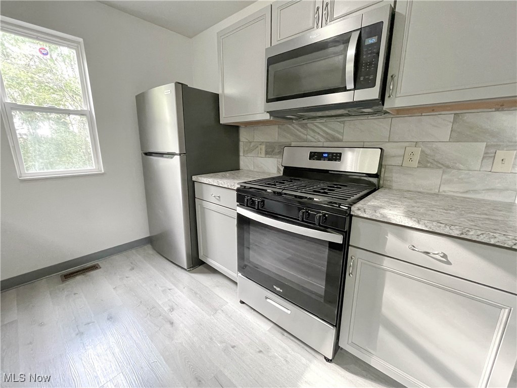 263 Reed Avenue Campbell, OH 44405 - Photo 10 of 30 Kitchen with gray cabinets, appliances with stainless steel finishes, light wood-type flooring, and tasteful backsplash