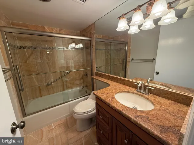 a bathroom with a granite countertop sink a toilet a mirror and shower