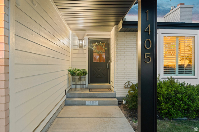 1405 Vintry Lane Murray, UT 84121 - Photo 5 of 44 Covered entryway featuring a dark wood-finish door with glass inserts, an exterior sconce, and a contrasting light brick facade