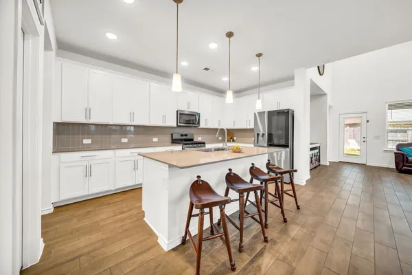 a kitchen with stainless steel appliances kitchen island granite countertop a stove a sink a refrigerator and white cabinets with wooden floor