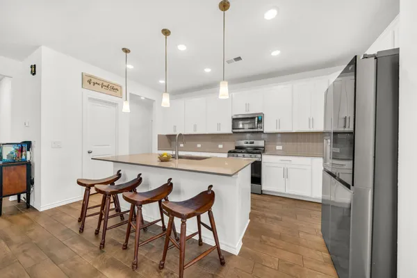 a kitchen with stainless steel appliances granite countertop a sink a stove a refrigerator and white cabinets with wooden floor