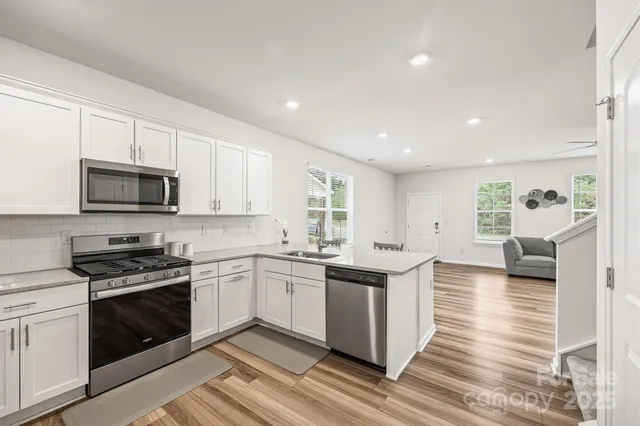 a kitchen with stainless steel appliances granite countertop a stove top oven a sink dishwasher and white cabinets with wooden floor