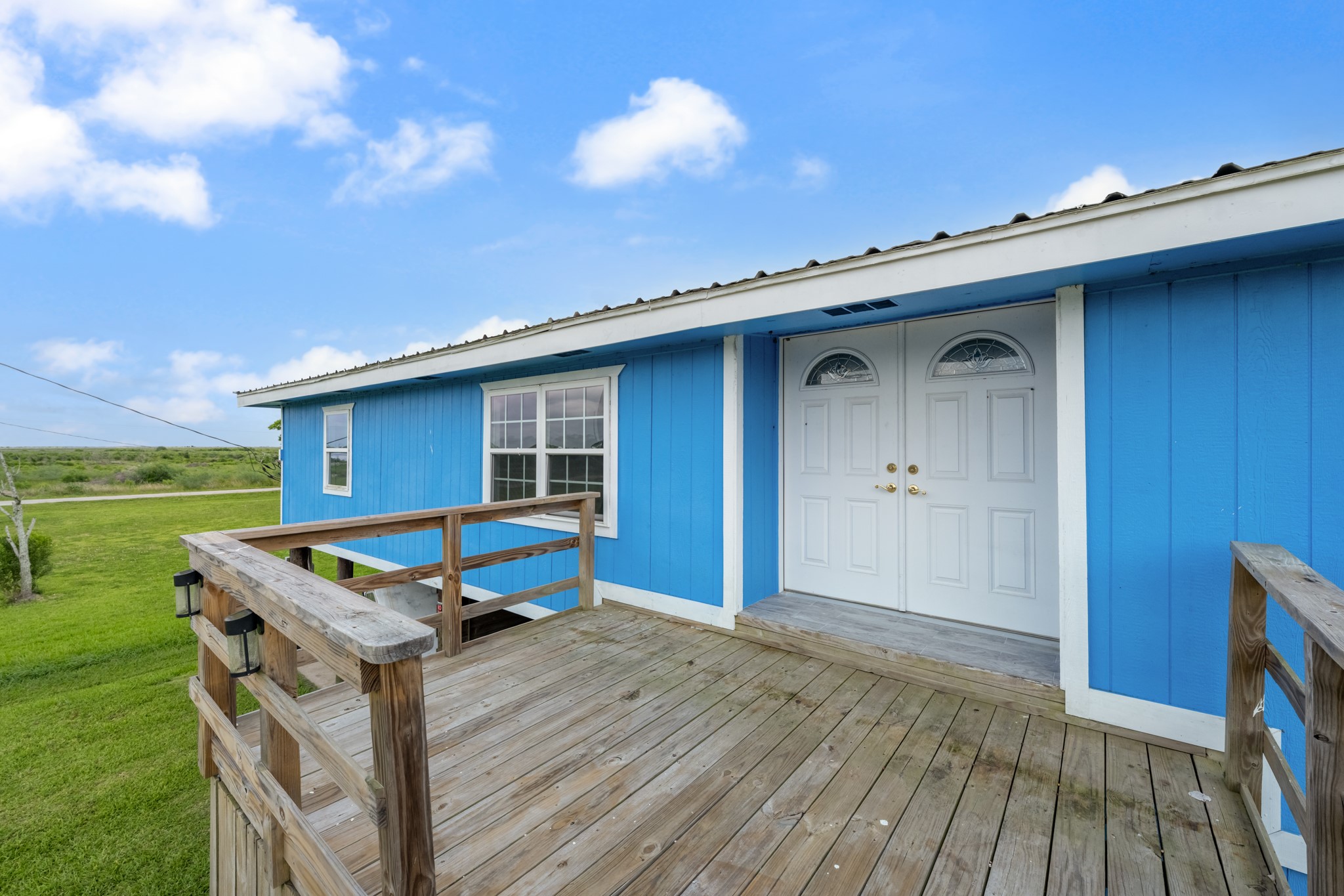 2534 Bastrop Angleton, TX 77515 - Photo 4 of 50 Welcoming elevated front entry with a spacious wood deck, ideal for enjoying peaceful country views and outdoor seating. Bright exterior finishes and double front doors create inviting curb appeal with a relaxed coastal feel.