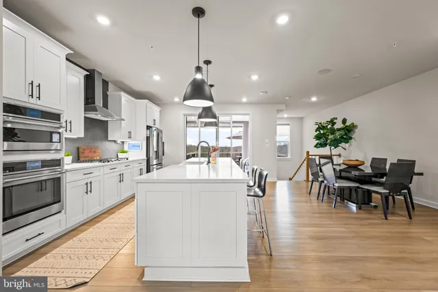 a kitchen with stainless steel appliances kitchen island granite countertop a stove top oven a sink a dining table and chairs with wooden floor