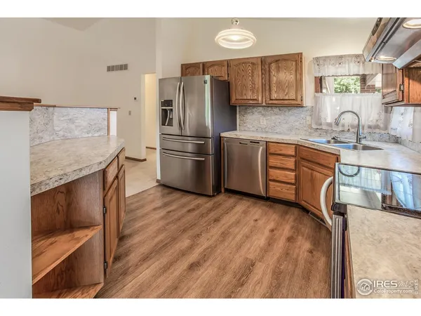 a kitchen with stainless steel appliances granite countertop a refrigerator a sink dishwasher and wooden cabinets with wooden floor