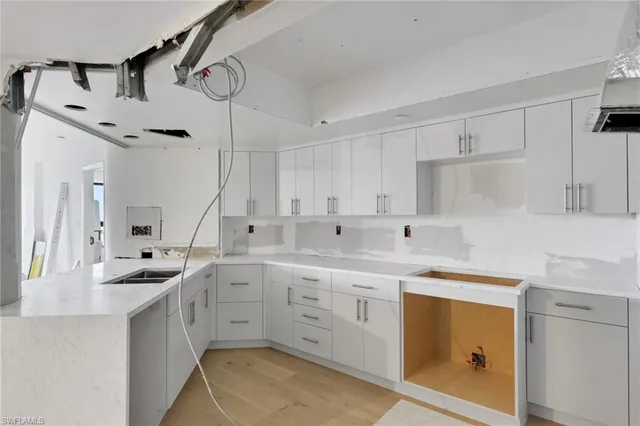a kitchen with a sink dishwasher and white cabinets with wooden floor