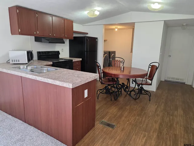 a kitchen with stainless steel appliances granite countertop a table chairs a refrigerator a stove a sink and dishwasher with wooden floor