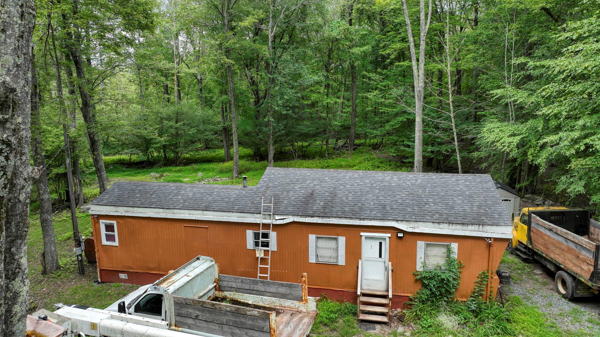 Back of property featuring crawl space, a view of trees, roof with shingles, and entry steps
