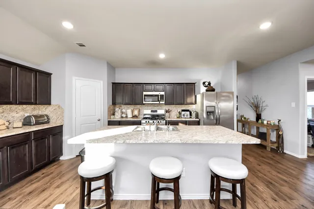 a kitchen with stainless steel appliances granite countertop a sink a stove a kitchen island with chairs and wooden floor