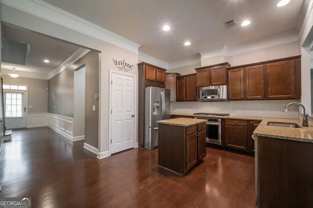 a kitchen with stainless steel appliances granite countertop wooden cabinets a refrigerator a sink a stove a microwave and wooden floors