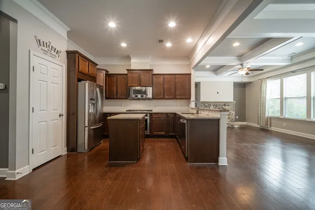 a kitchen with stainless steel appliances granite countertop a refrigerator a sink dishwasher a stove top oven a large island with wooden floor and cabinets
