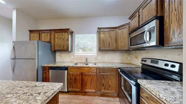 a large kitchen with granite countertop a large counter top stainless steel appliances a sink and a window