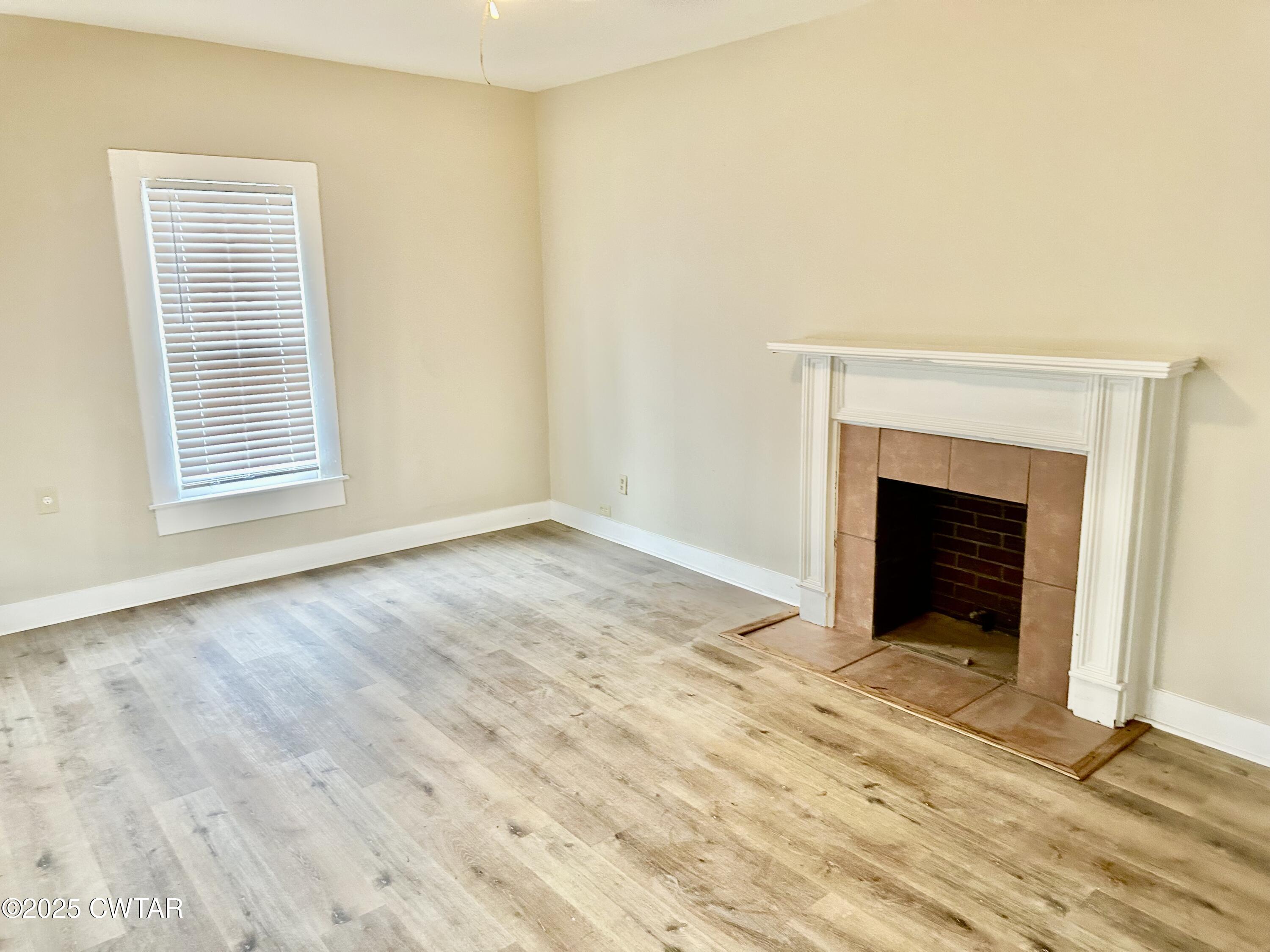 1509 Vine Street Humboldt, TN 38343 - Photo 3 of 9 a view of an empty room with wooden floor fireplace and a window