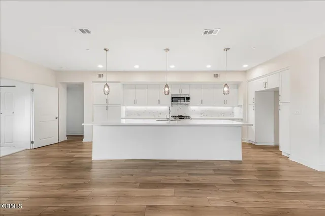 a large white kitchen with kitchen island a sink wooden floor and a refrigerator