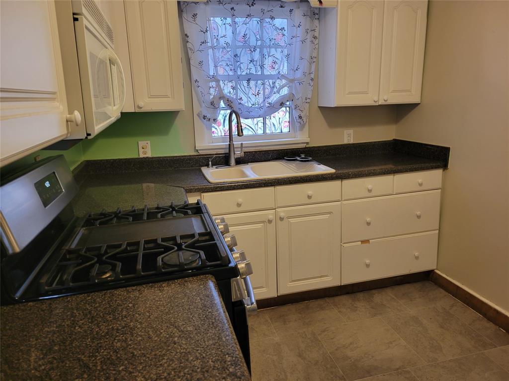 211 Wichita Street Shreveport, LA 71101 - Photo 3 of 10 Kitchen featuring dark countertops, stainless steel gas stove, white microwave, and white cabinets