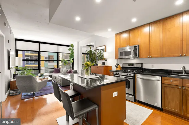 a open kitchen with stainless steel appliances granite countertop a stove top oven a sink dishwasher a dining table and chairs with wooden floor