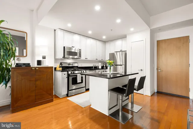 a kitchen with stainless steel appliances kitchen island granite countertop a stove a sink dishwasher a refrigerator and a dining table with wooden floor